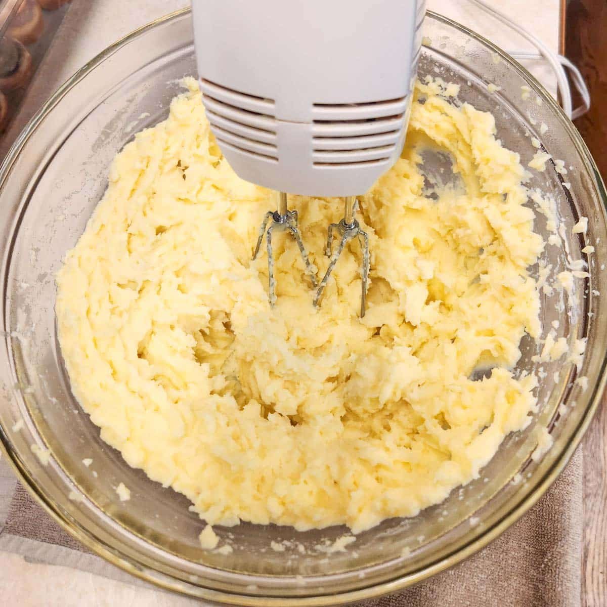 Hand mixer in a bowl of creamy garlic mashed potatoes.