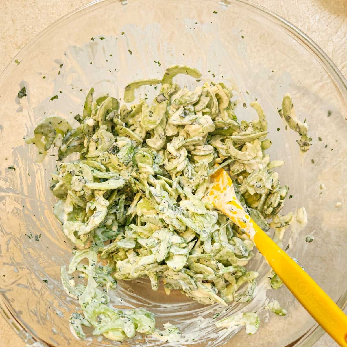 Spoon resting in celery blue cheese slaw in a mixing bowl.