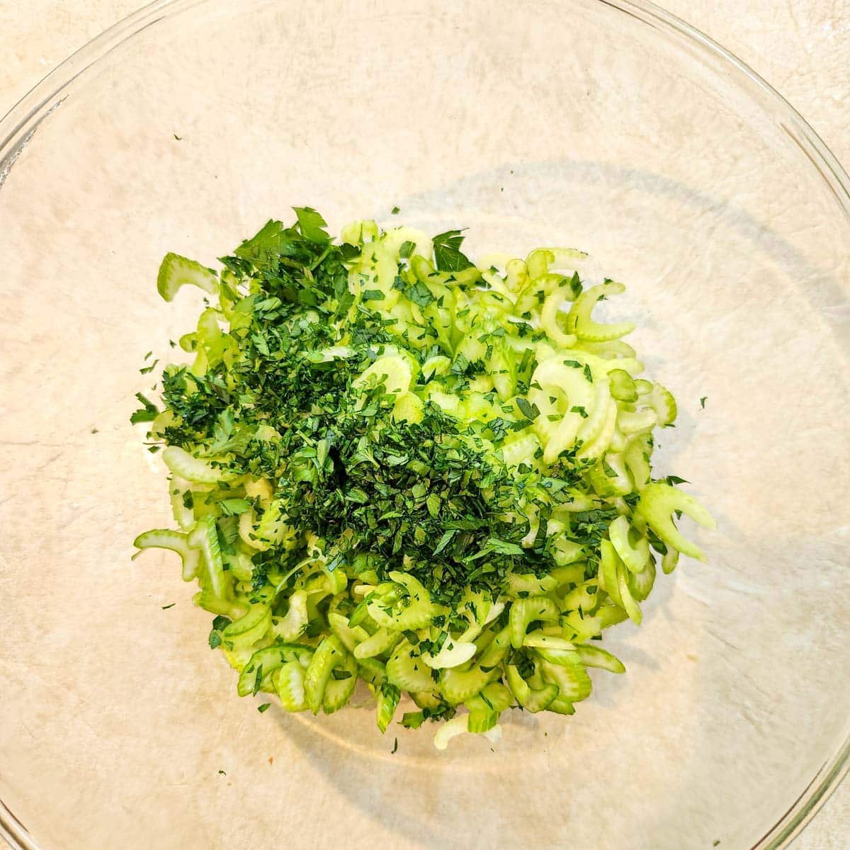 Thinly sliced celery and chopped parsley added to a mixing bowl.