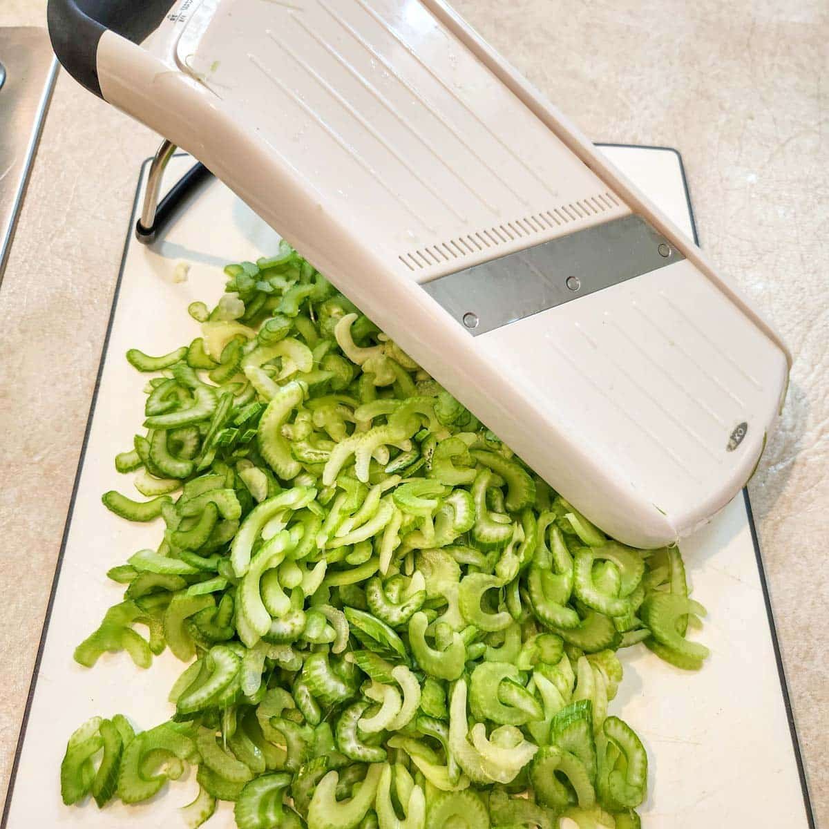 Mandolin slicer with thin sliced celery on the cutting board.