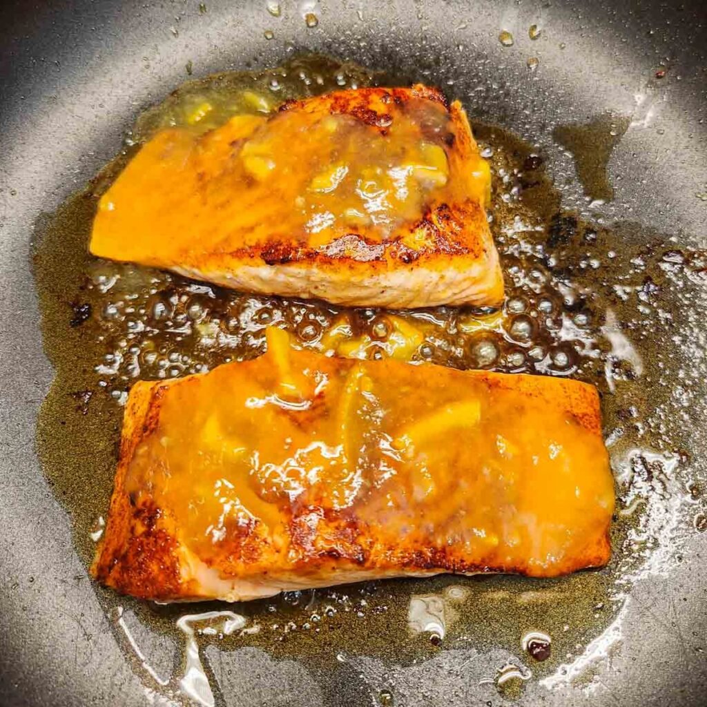 Seasoned salmon filets in a skillet topped with a glaze.