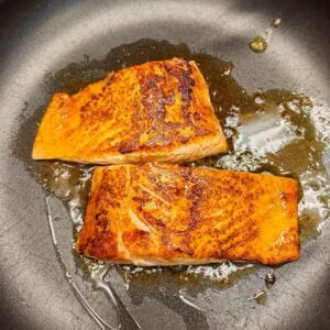 Hot oil in a skillet with golden brown salmon filets sauteing.