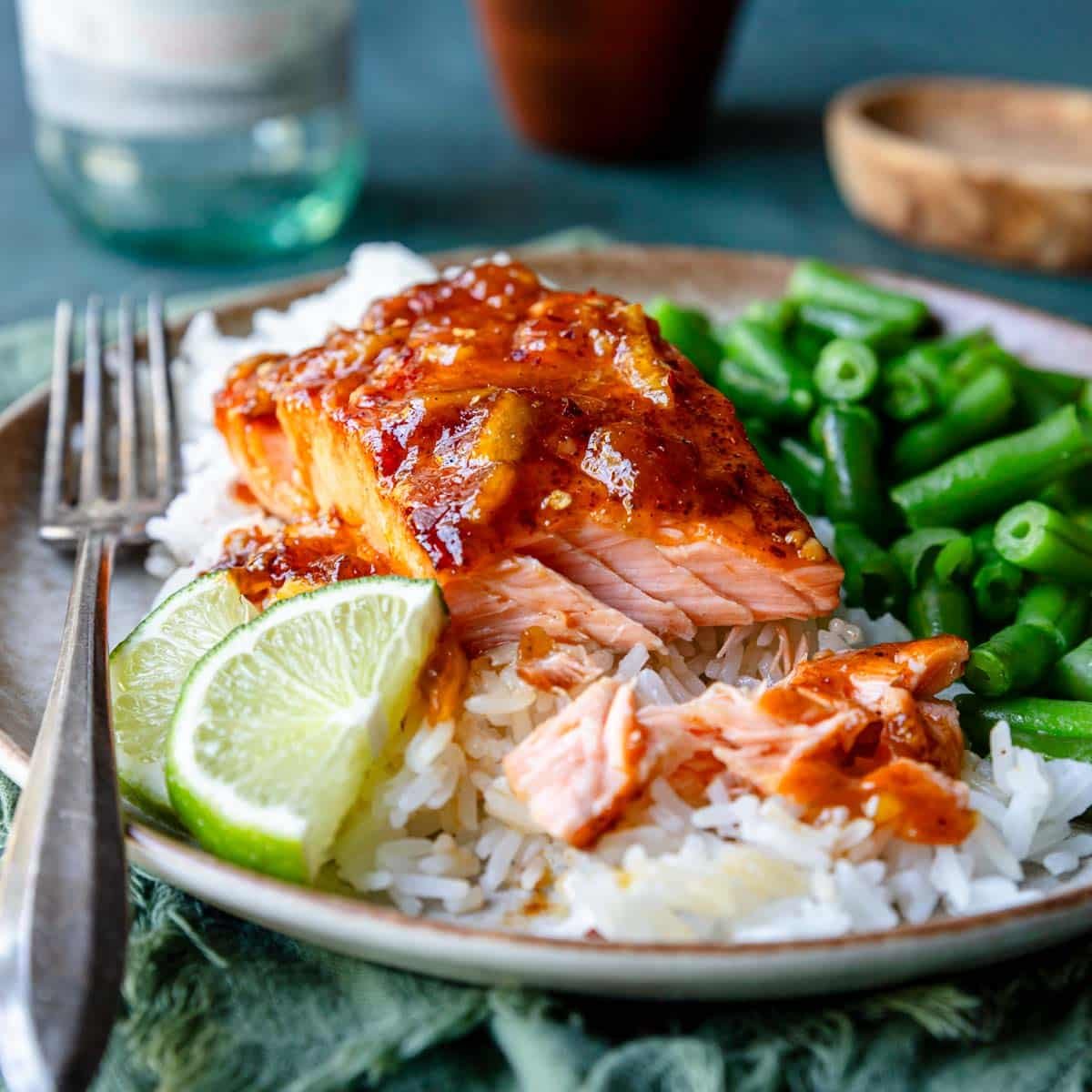 Flaky pieces of glazed salmon over partially eaten rice and green beans on a plate.