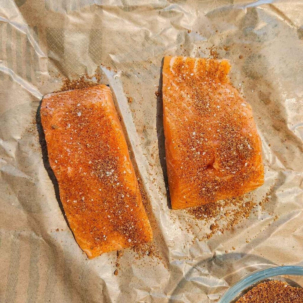 Raw salmon filets coated with homemade seasoning on parchment paper.