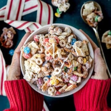 Hands holding a bowl of sweet white chocolate chex mix.