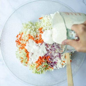 Susie pouring the sauce over the coleslaw ingredients in a mixing bowl.