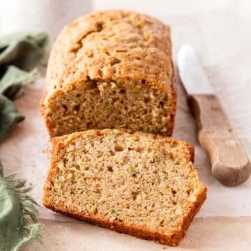 Close up of a loaf of zucchini bread and a slice laying in front of it to enjoy.