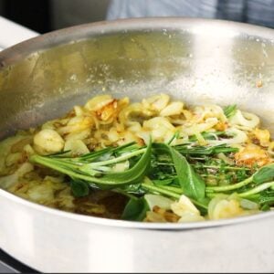 Celery and onions with fresh herbs in a skillet.