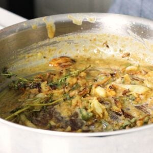 Flour coated veggies and fresh herbs being combined in a skillet.