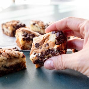 Hand picking up a chocolate chip cheesecake square bar.