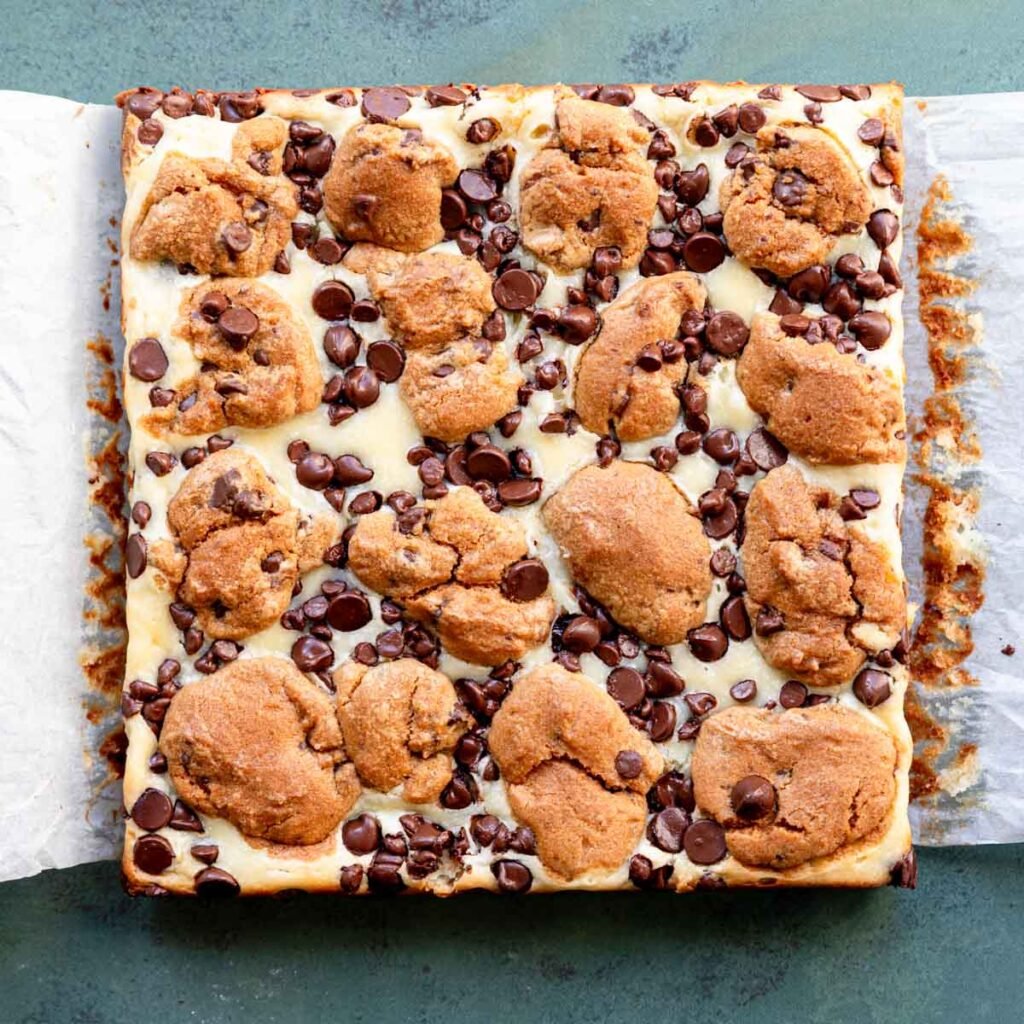 Top view of freshly baked chocolate chip cheesecake bars on parchment paper.