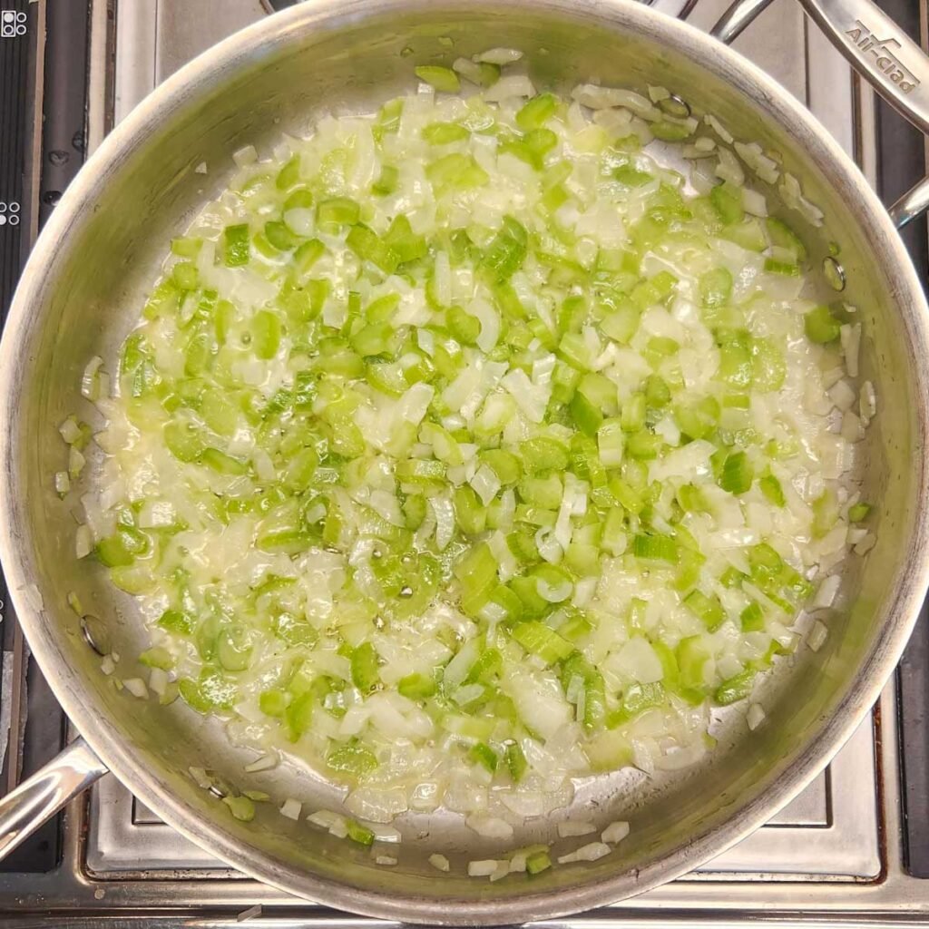 Skillet with onions and celery sauteing from a top view.