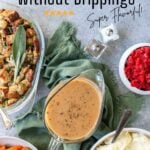 Pinterest image for turkey gravy without drippings showing the homemade sauce in a gravy boat with holiday side dishes in serving bowls around it like stuffing, roasted carrots and mashed potatoes.