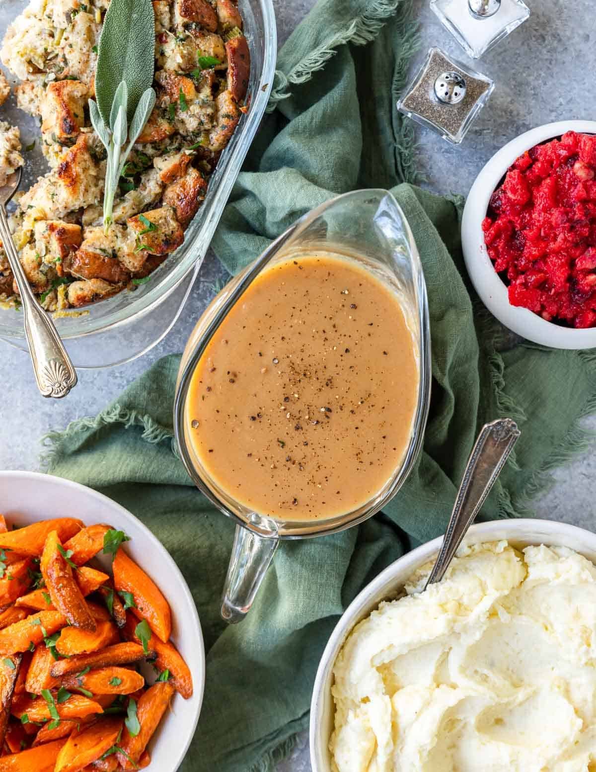 Turkey gravy in the middle of other holiday side dishes like mashed potatoes, stuffing and roasted carrots.