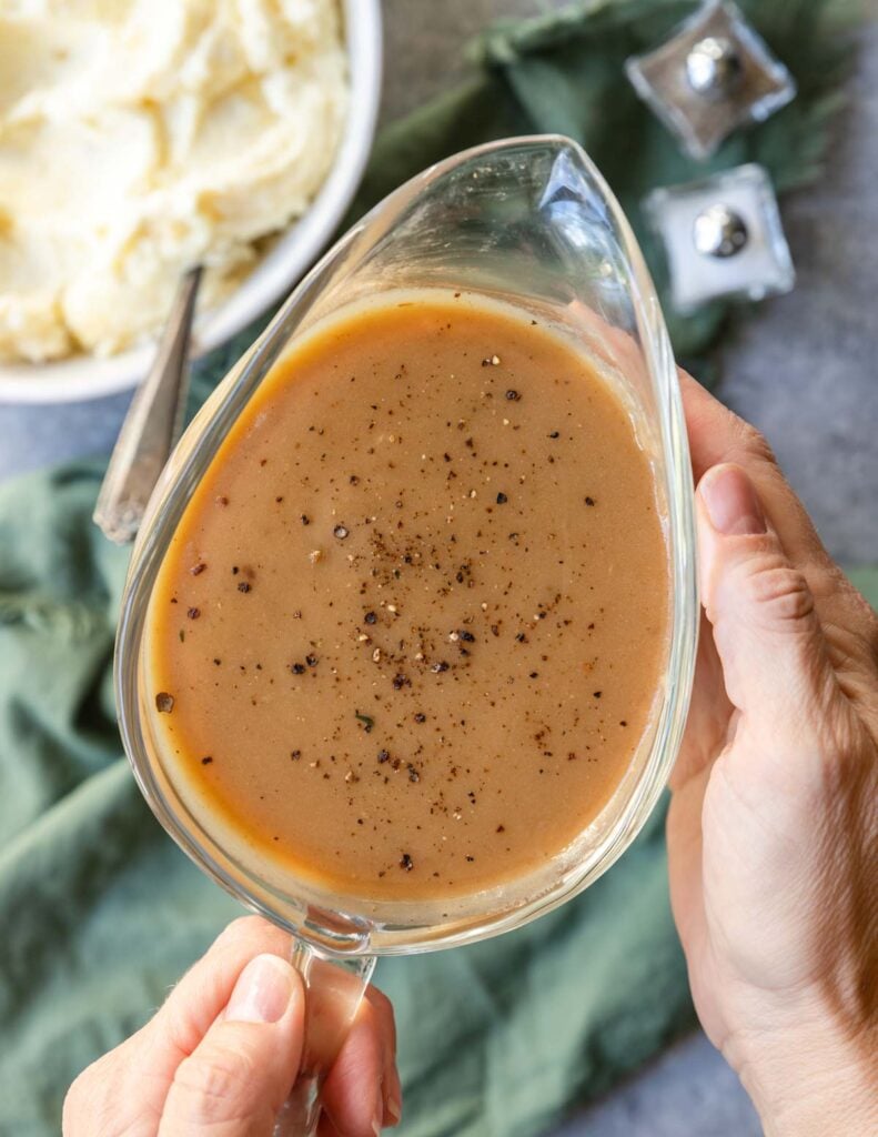 Hands holding a glass gravy boat filled with super flavorful turkey gravy without drippings.