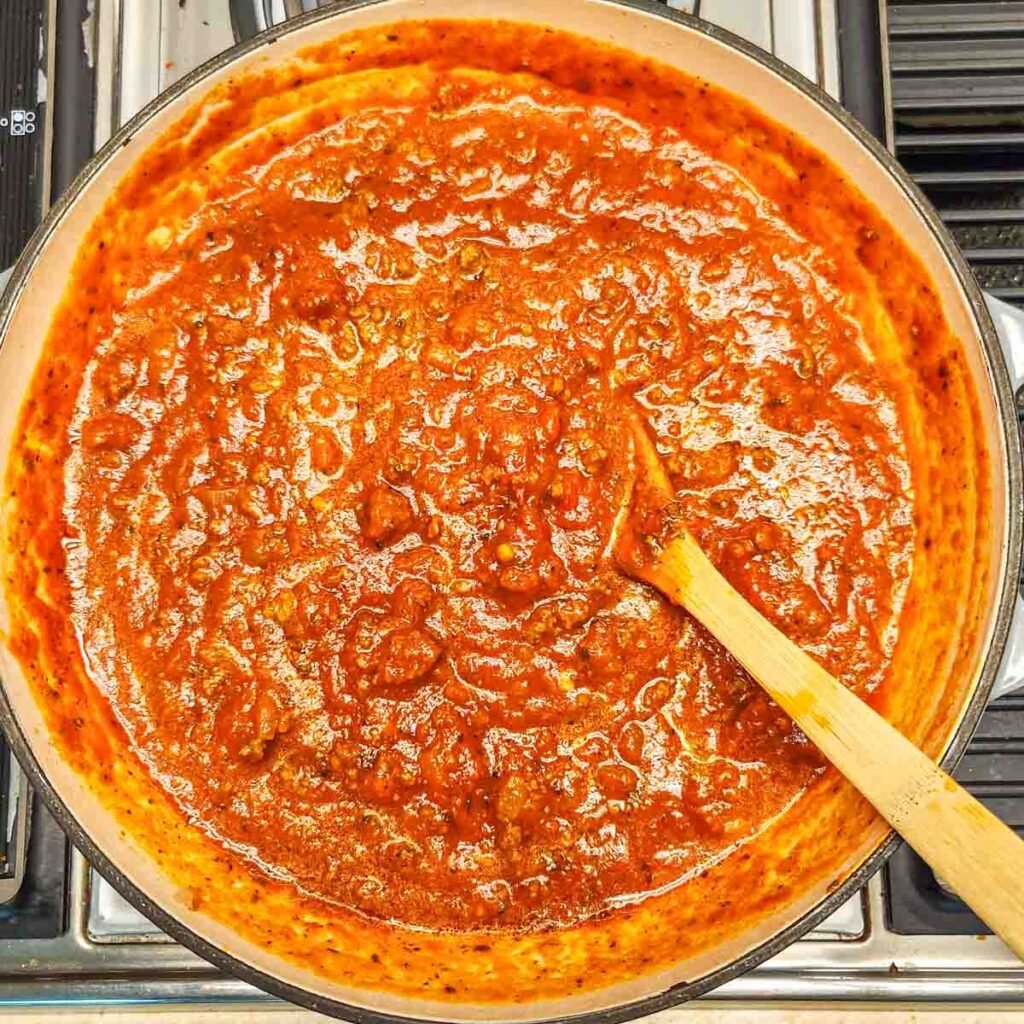 Pasta sauce with ground beef in a skillet with a wooden serving spoon.