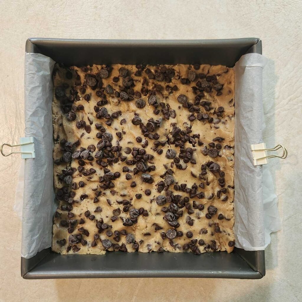 Extra chocolate chips added to the top of the cookie dough in the baking pan.