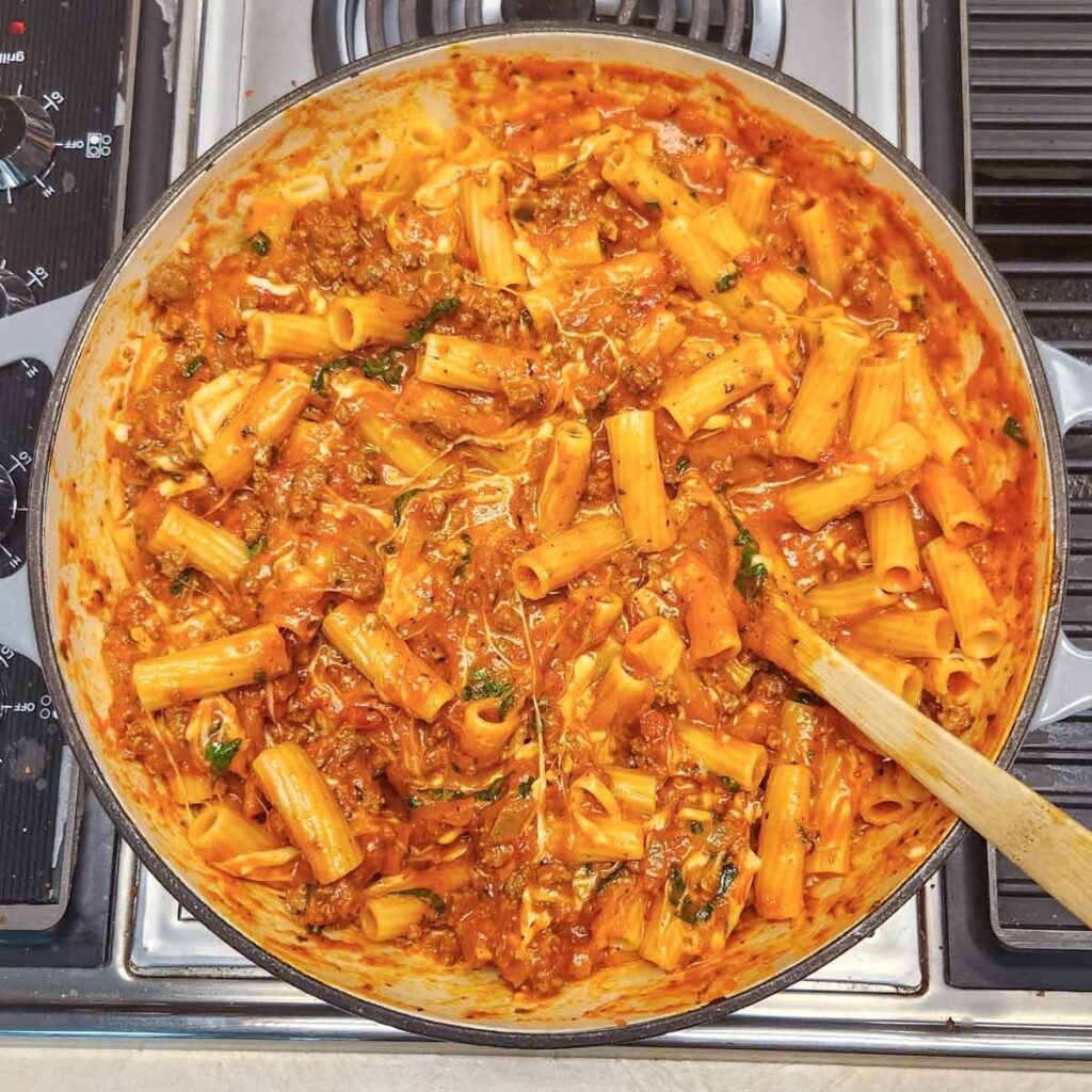 Gooey cheesy rigatoni coated with cheese and pasta sauce in a skillet.