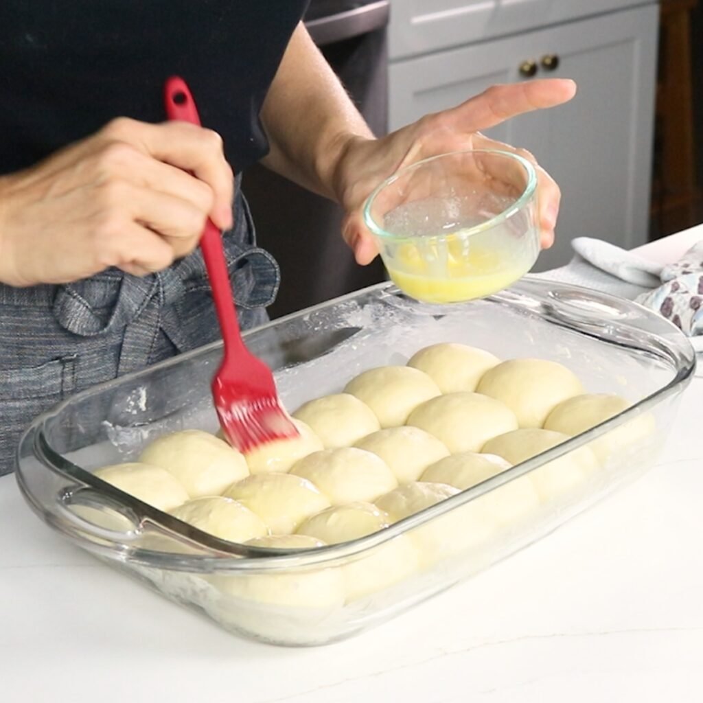 brushing dinner roll dough with melted butter, ready for the oven