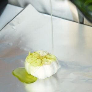 Olive oil being drizzled on garlic in a piece of foil.