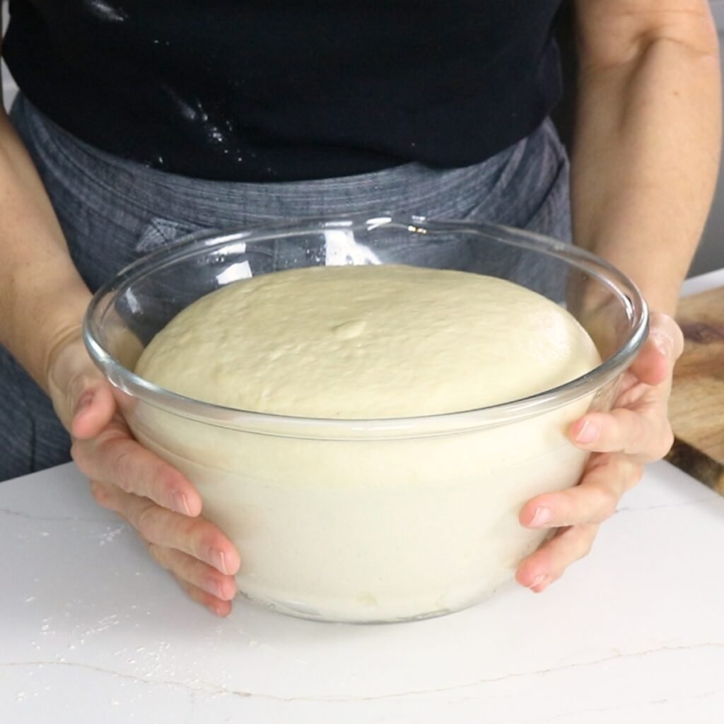 dinner roll dough that has doubled in size in a glass bowl.