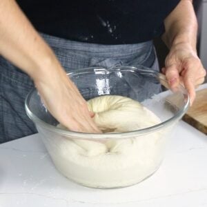 punching dough down in a glass bowl