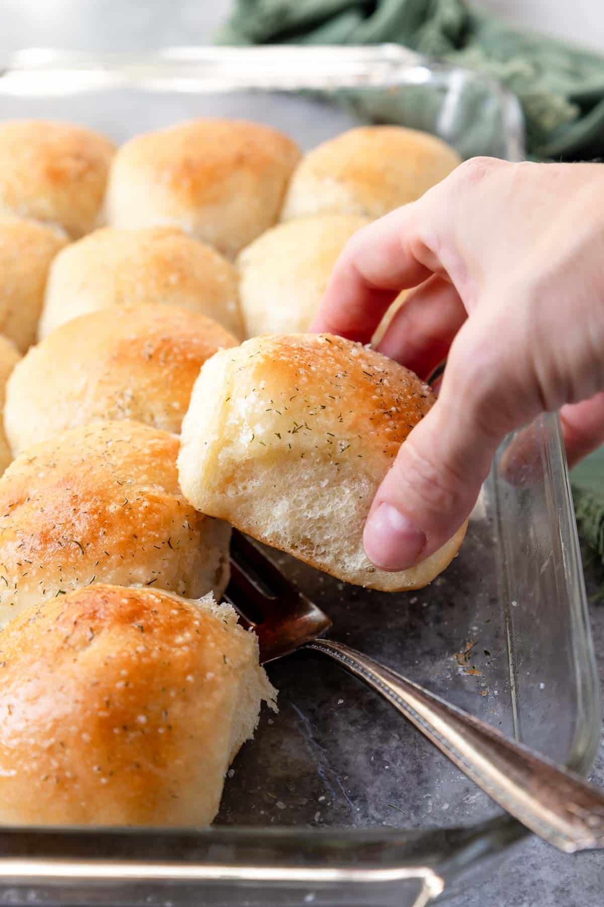 A fluffy dinner roll being pulled out of the baking pan 