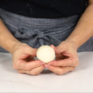 hands holding a smooth ball of dough for dinner rolls