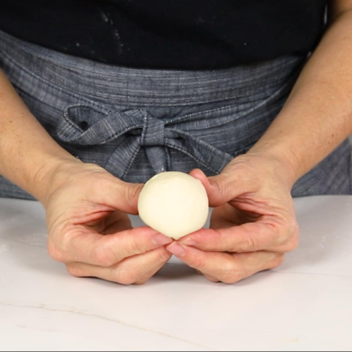 hands holding a smooth ball of dough for dinner rolls 