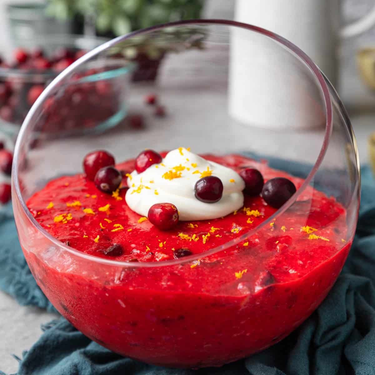 Cranberry jello salad in a glass bowl with whipped cream and whole cranberries garnished on top.