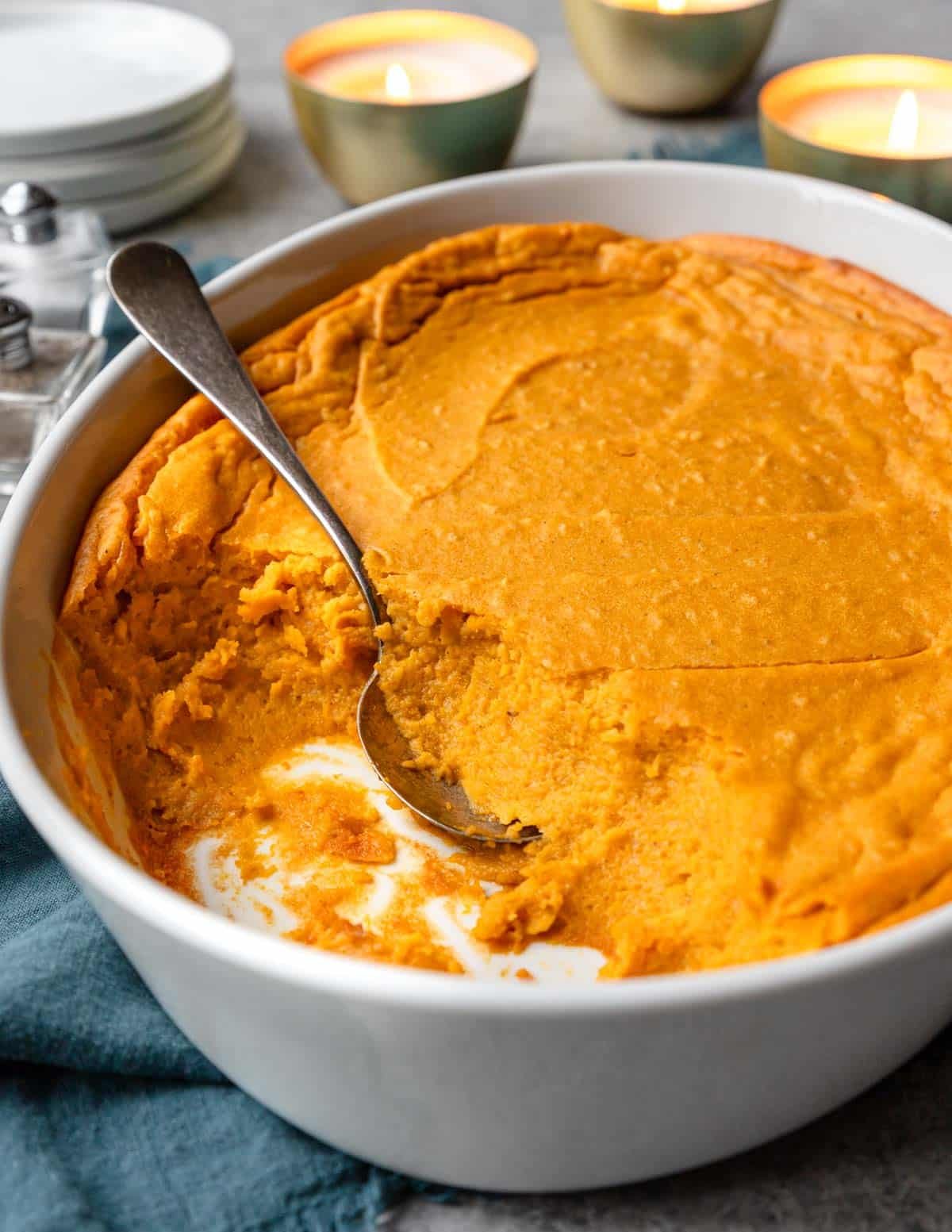 a 2 quart casserole pan with a sweet potato souffle baked inside, some is scooped out with a spoon laying on the side.