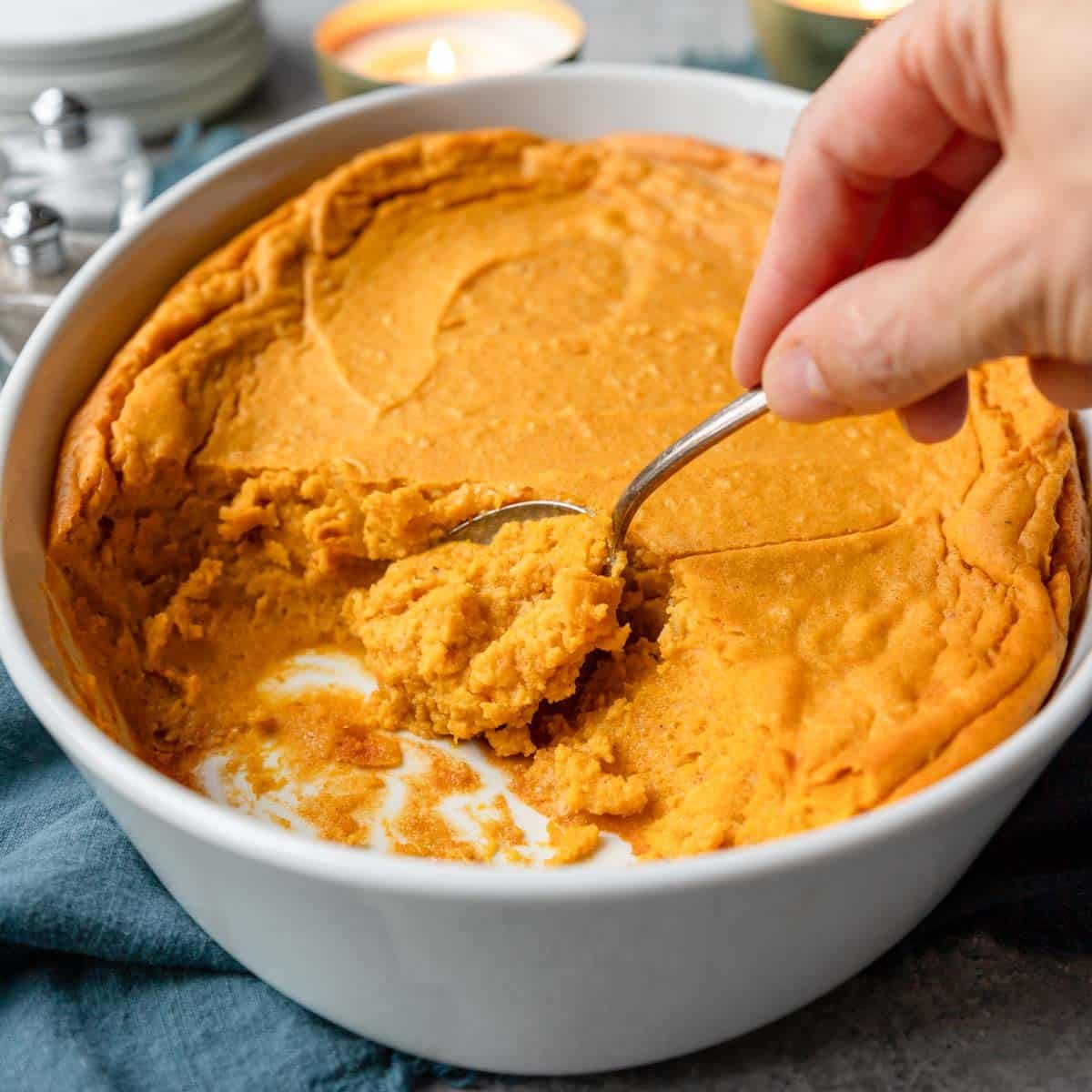 A sweet potato souffle in a 2 quart casserole pan and a spoon dishing some out.