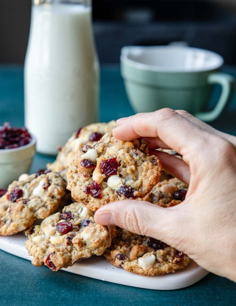 a hand grabbing a cookie that has cranberries, pecans and white chocolate chips in it.