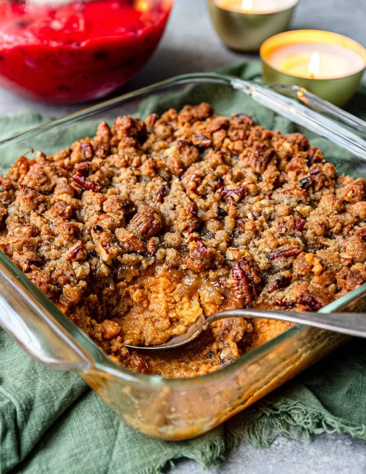 sweet potato casserole in an 8x8 pan with pecan brown sugar topping and cranberries in the background