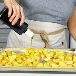 Oil being poured over chopped Yukon potatoes on a foil covered baking sheet.