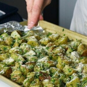 Parmesan cheese being sprinkled over herb roasted potatoes on a baking sheet.