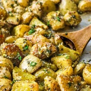 Herb roasted potatoes being scooped up on wooden serving spoon.