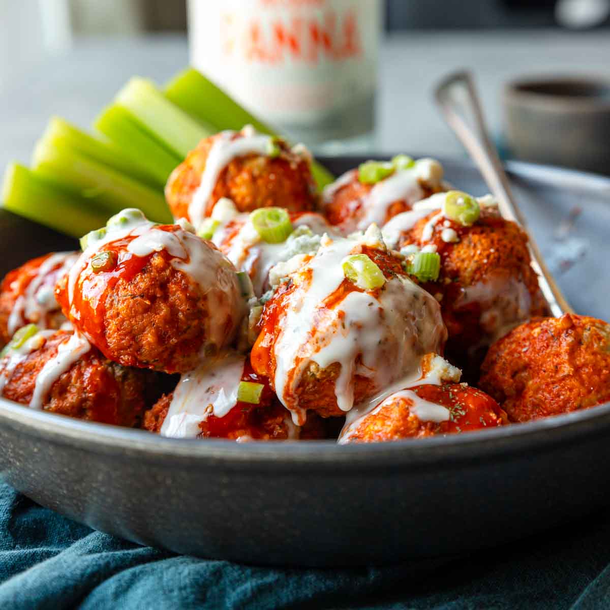 Buffalo Chicken Meatballs in a bowl topped with green onions, Ranch and a few celery sticks on the side.