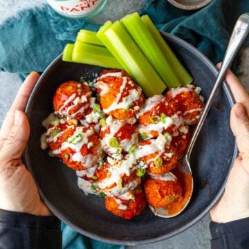 two hands holding a bowl of buffalo chicken meatballs with celery on the side.