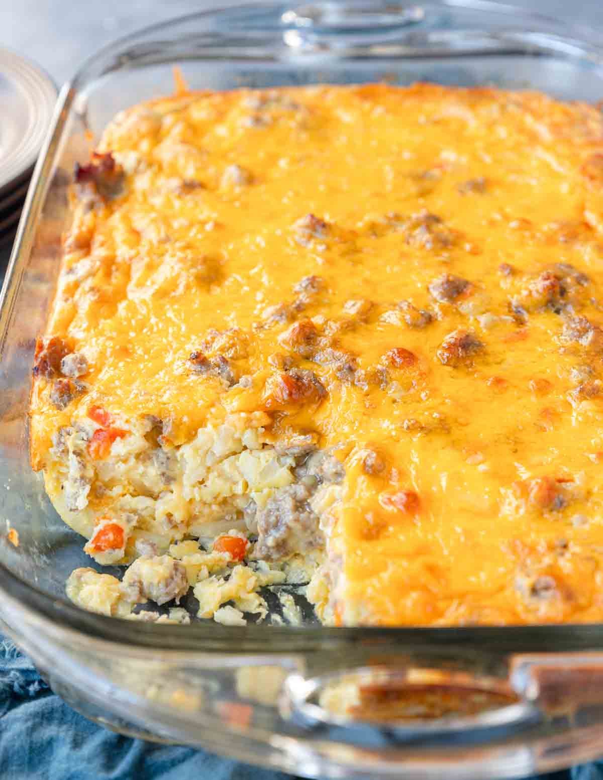 Close up of a sausage breakfast casserole with a slice removed to show the egg mixture combined with diced red peppers, ground pork and shredded hashbrowns.