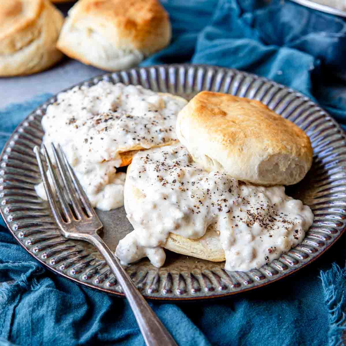 Halved biscuits on a plate, topped with sauage gravy recipe with a fork resting on the side.