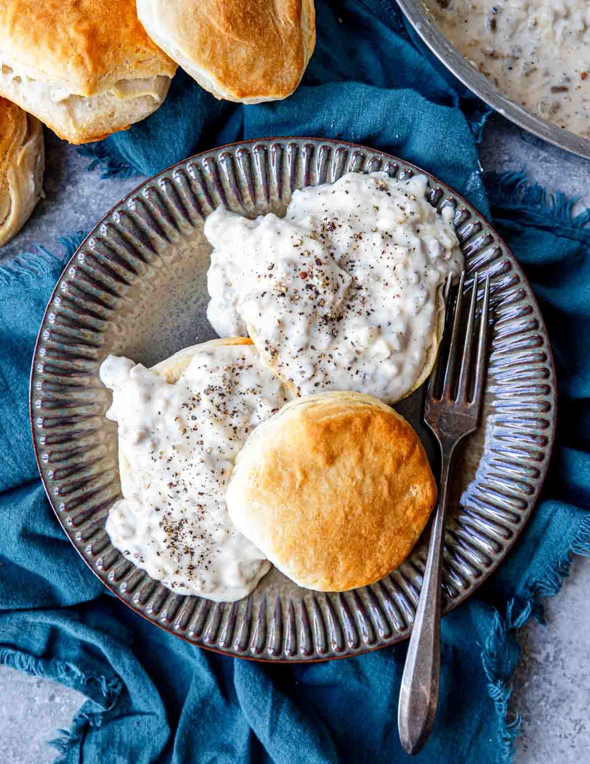 Top view of a plate filled with sausage gravy on top of halved freshly baked biscuits.