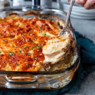 a glass casserole dish with scalloped potatoes being spooned out.