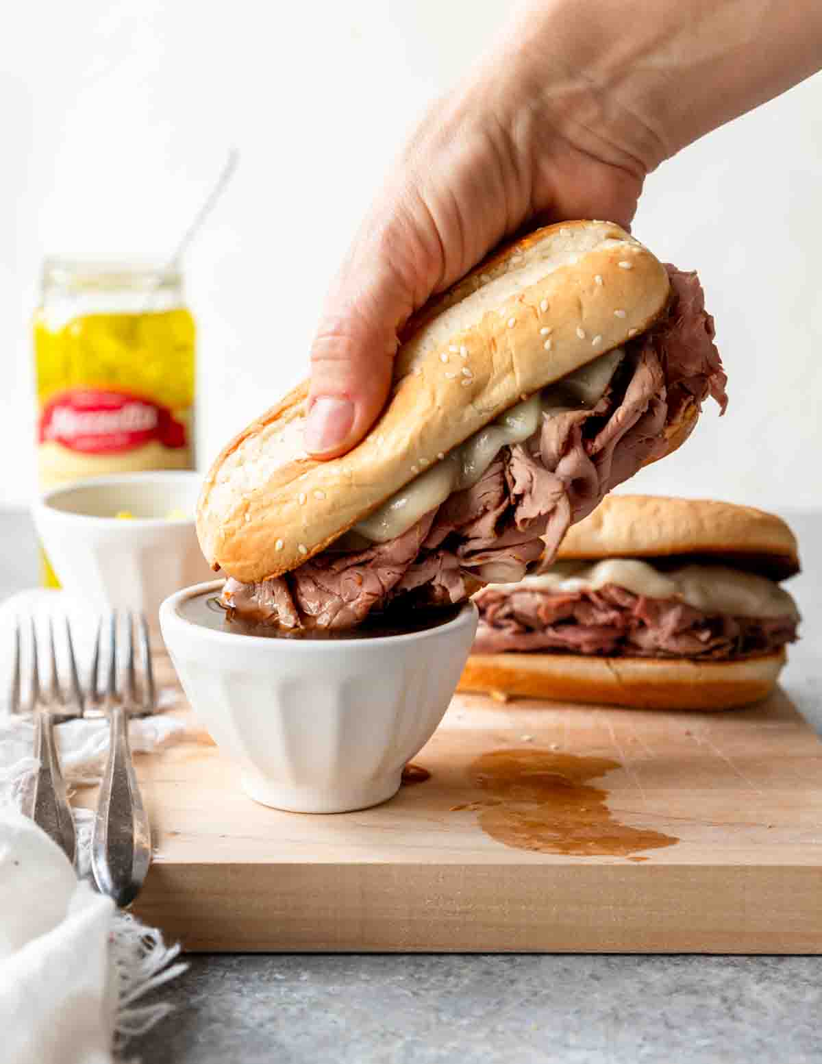 Hand dunking a melted cheesy French dip sandwich into a small bowl of au just.