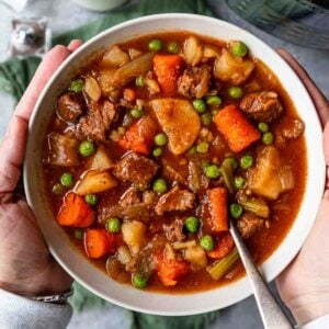 Close up of Instant Pot Beef Stew with a spoon resting in the mixture, showing carrots, beef chunks, peas, and potatoes.