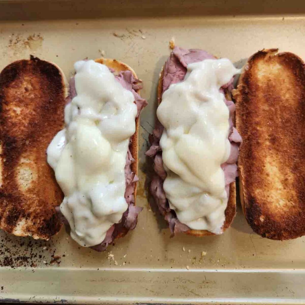 Toasted sub buns topped with sliced beef and topped with cheese that's melted over the top.