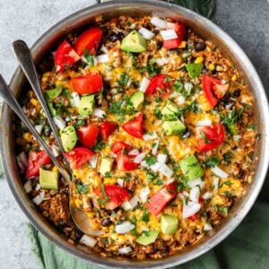 Taco skillet served with chopped tomatoes, onions. avocado pieces and chopped cilantro garnishing the family meal.