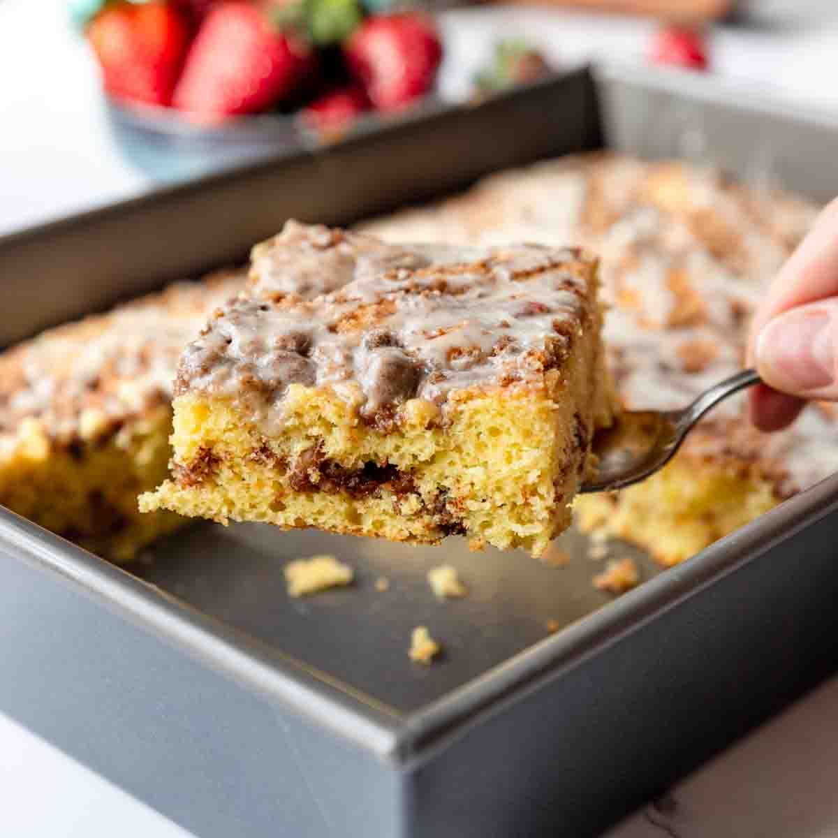 A slice of cake mix coffee cake topped with a vanilla icing, being served out of the baking pan.
