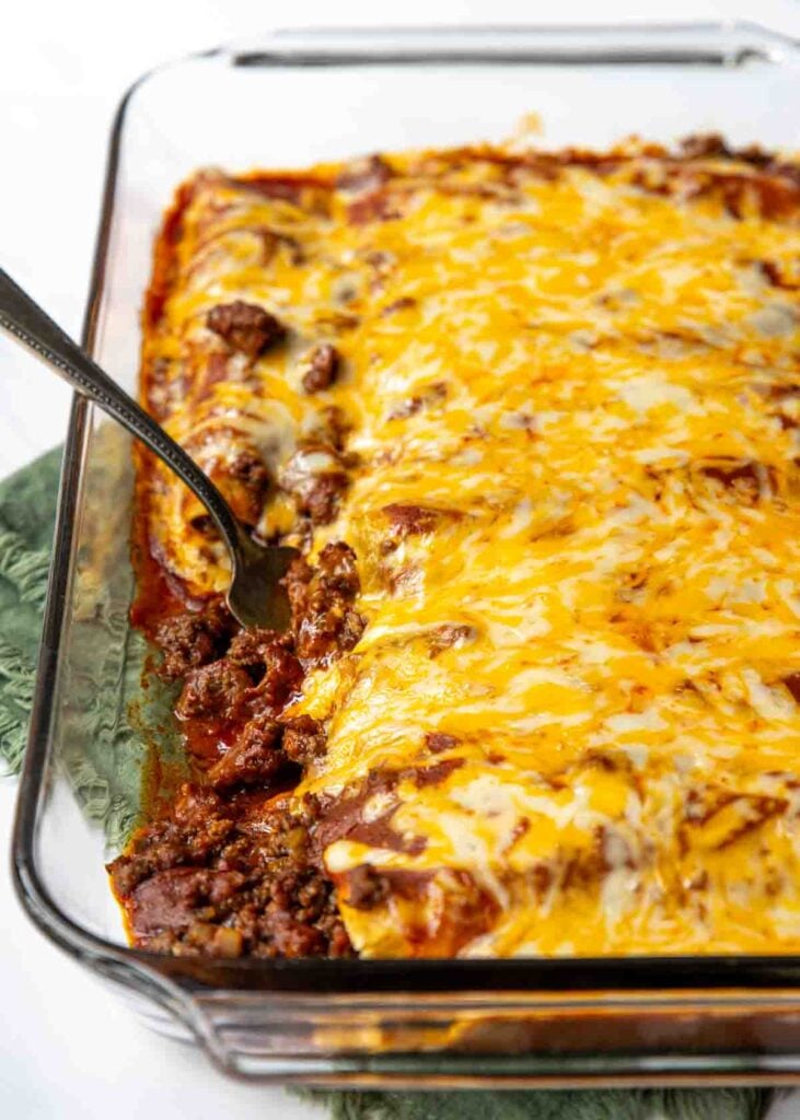 Ground beef mixture spilling out of corn tortillas in a baking dish on enchilada sauce with melted cheese over the top.