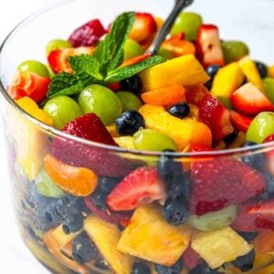 A large bowl of fruit salad topped with a sprig of mint